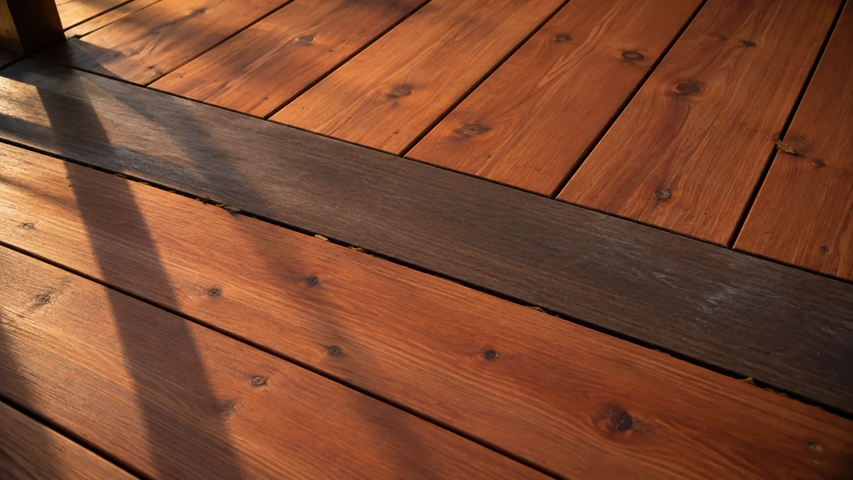 Warm red brown cedar decking meeting a darker tropical hardwood border board in low evening light